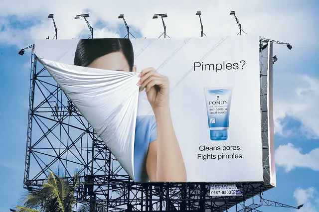 Billboard advertisement with a large image of a person pulling a white cloth over half of the face, revealing only one eye, with a product by POND'S displayed alongside the text 'Pimples? Cleans pores. Fights pimples.'